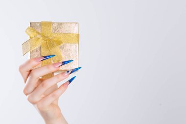 Hediye kutusu. Modern stil mavi stil çivi cilası. Güzel eller altın hediye kutusunu tutuyor. Renkli Fransız donanma çivileri izole edilmiş beyaz arka plan. Tırnak cilası. Sanat Manikürü. 