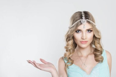 Beauty Queen bride woman with bright pink with tikka indian jewelry on head looking at you camera showing to side wards copy space with hand,  light bridal makeup isolated grey white background wall