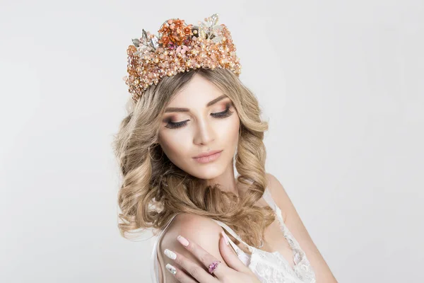 Beautiful blonde girl in a golden crown on white grey background, eyes closed looking down hand on shoulder pink ring on it — ストック写真