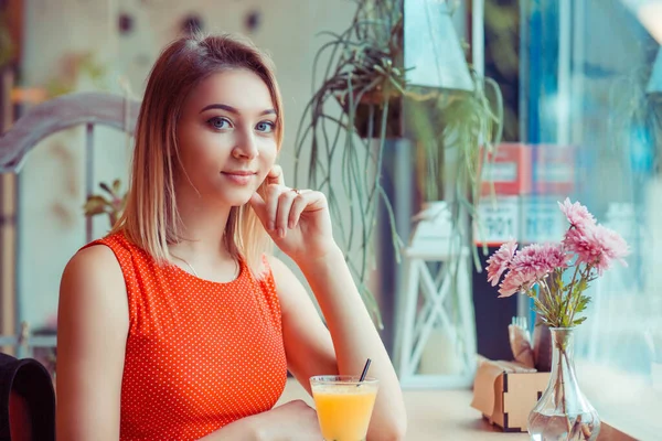 Chica feliz desayunando con jugo de naranja en una cafetería en casa cerca de la ventana y mirando a la cámara —  Fotos de Stock