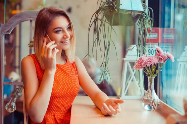 Πορτρέτο του ένα αστείο κορίτσι, λαμβάνοντας μια τηλεφωνική συνομιλία κάθεται σε ένα τραπέζι στο σπίτι και ψάχνει μέσα από το παράθυρο — Φωτογραφία Αρχείου