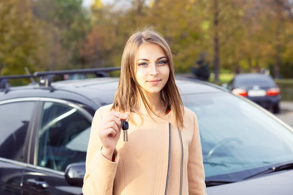 Closeup portrait serious young attractive woman, buyer near her new car showing keys isolated outside dealer, dealership lot office. Personal transportation, auto purchase concept — Stock Photo, Image