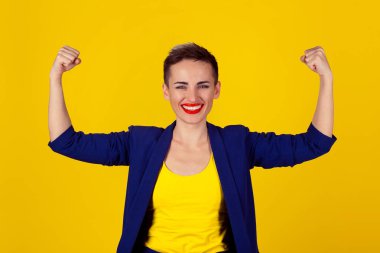 Güçlü ve mutluyum. Sarı arka planda gücünü gösteren mutlu ve zarif bir iş kadınının portresi. Çok kültürlü Latin bir kız kısa saçlı, kırmızı dudaklı, mavi takım elbiseli, sarı gömlekli.