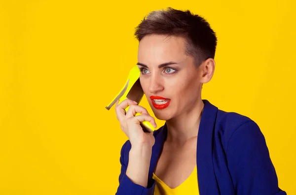 Kobieta krótkie włosy trzymając limonkowy kolor obcas telefon komórkowy telefon komórkowy symulujący rozmowę na nim odizolowane żółte tło — Zdjęcie stockowe