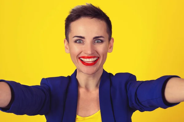 Feliz, foto selfie. Primer plano excitado mujer pelo corto chica sonriendo mientras hace selfie en la cámara del teléfono móvil en amarillo. Emoción positiva de expresión facial. Divertido concepto de ocio alegría —  Fotos de Stock