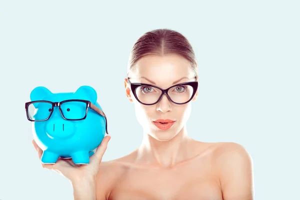 Glasses sale concept. Happy woman holding piggy bank both wearing eye wear glasses. Female model isolated light blue white background. — Stock Photo, Image