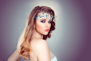 Ona güzelliğini göstererek geri dönüyor. Güzel makyajı, gençliği ve cilt bakımı konsepti olan güzel bir kız. Gri arka plandaki çekici sarışın kızın fotoğrafı.