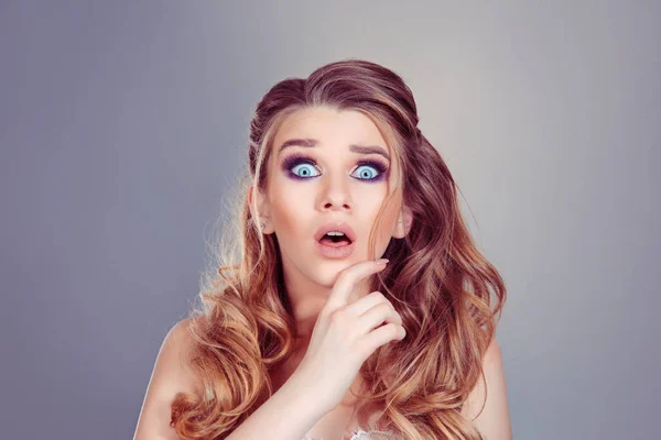 Shocking news. Beautiful shocked surprised curly blonde woman girl with big eyes with open month looking at camera isolated on a gray purple background with copy space