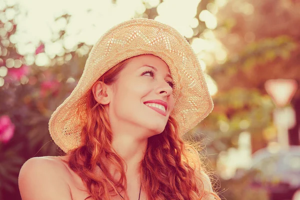 Chica feliz. Mujer con sombrero mirando hacia los lados sonriendo feliz arbusto verde aislado con flores rosadas en el fondo. Filtro rojo tonificado retro . — Foto de Stock