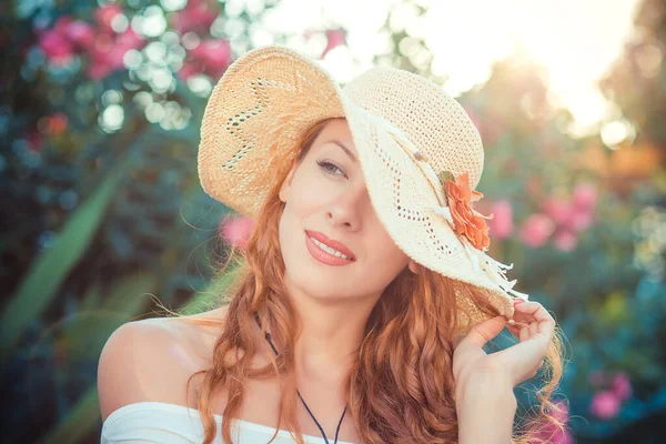 Pensive relaxed girl daydreaming thinking about love in straw hat looking forward at sunset isolated on green bush shrub pink flowers background — Stock Photo, Image