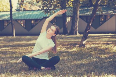 Parktaki yeşil çimenler üzerinde esneme egzersizi yapan güzel bir genç kadın. Yoga egzersizi..