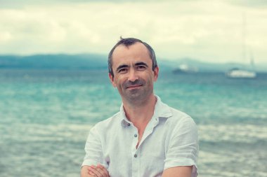 Orta yaşlı bir adam yazın sahilde dişsiz gülümsüyor.