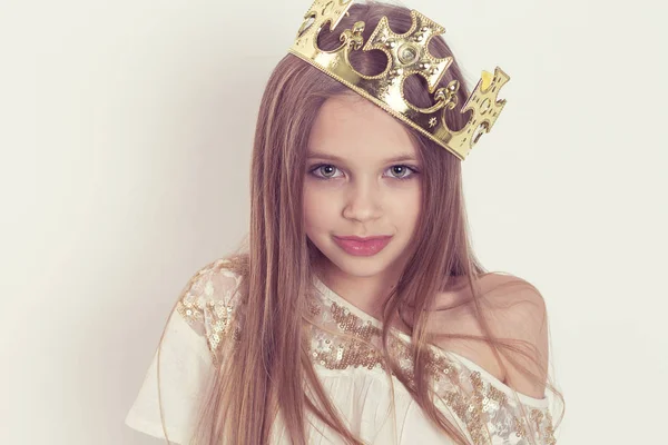 Jong meisje kind met een leuke glimlach het dragen van een kroon en een wit lovertje jurk op vakantie verjaardag partij geïsoleerd op witte achtergrond muur kijken naar je camera poseren — Stockfoto
