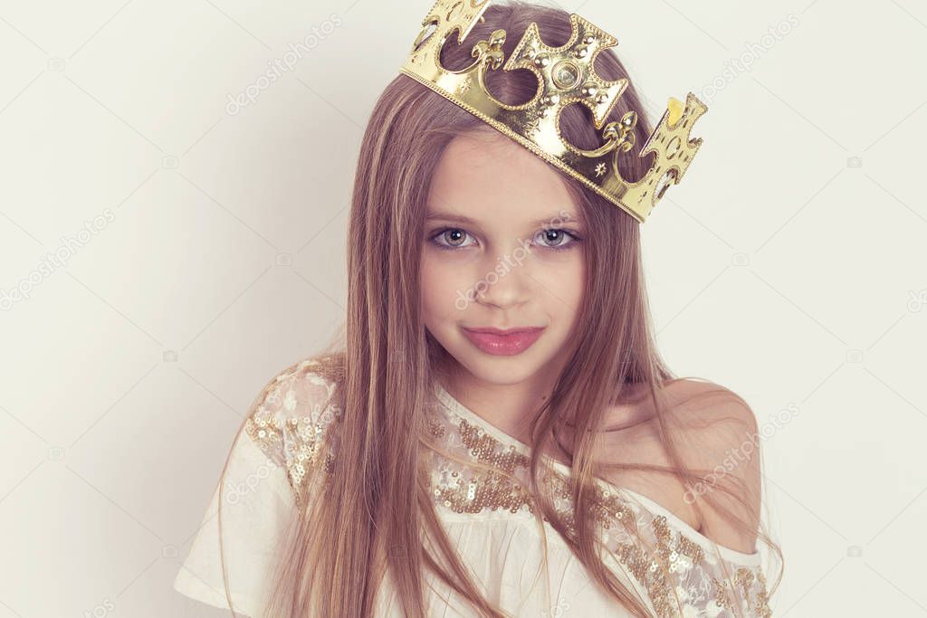 Young girl kid with a cute smile wearing a crown and a white sequined dress on Holiday birthday party isolated on white background wall looking at you camera posing
