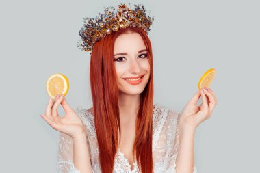 Bayan ve C vitamini. İki dilim portakal tutan genç bir kadın. Elinde iki dilim portakal tutan genç bir kadın. Kafasında kristal taç olan güzel bir kadın. Açık gri renkte izole edilmiş.