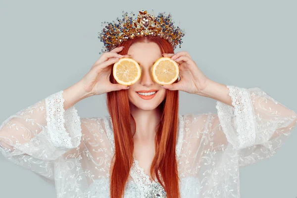 Vitamine C et beauté. Une jeune femme tenant les yeux couvrants avec deux tranches de citrons orange comme masque de peau de la région des yeux jolie femme avec couronne de cristal sur la tête isolée sur gris clair — Photo