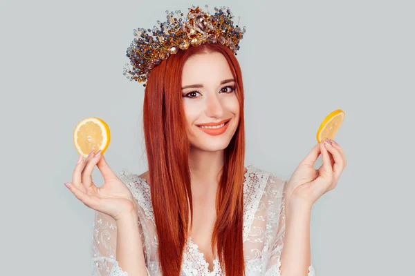Королева краси і Вітамін С. Молода жінка тримає два скибочки апельсинів. Молода жінка тримає два скибочки апельсинів красива жінка з кришталевою короною на голові ізольовано на світло-сірому — стокове фото