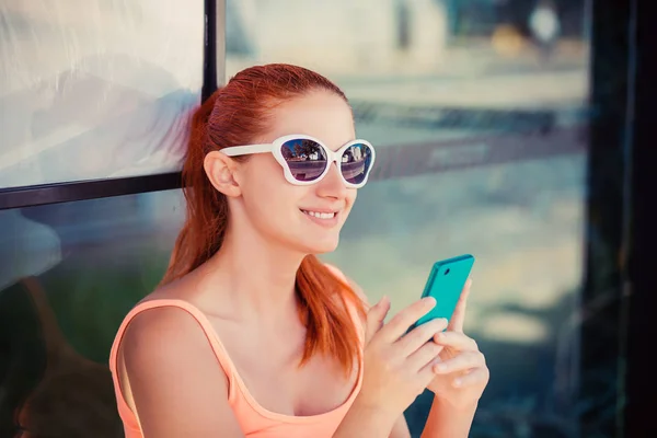 Boas notícias por telefone. Mulher bonita olhando para o telefone ao ar livre na estação de ônibus sorrindo sorriso de dente usando o aplicativo para rastrear o horário de ônibus — Fotografia de Stock