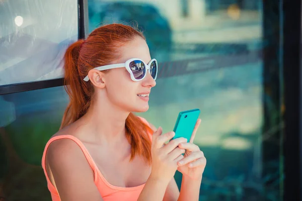 Mulher bonita sentada na estação de ônibus segurando telefone celular — Fotografia de Stock