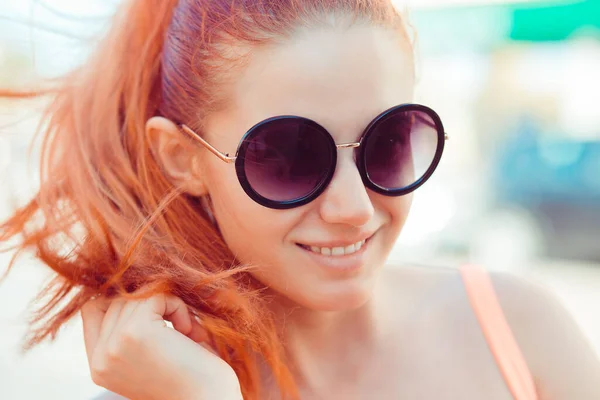 Kasabada mutluyuz. Güzel kızıl saçlı kadın arka planda kameraya gülümsüyor. — Stok fotoğraf