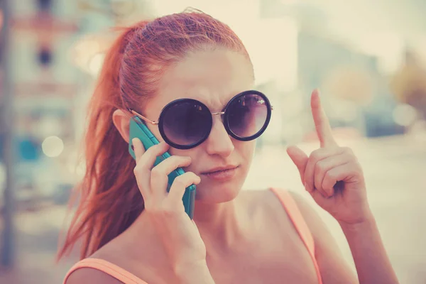 Attention, listen to me. Close up portrait of young unhappy frustrated woman wagging finger talking at phone on city scape background. — 스톡 사진