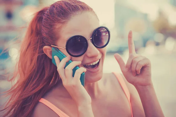 SMS. Closeup portrait happy pleased young girl having idea pointing up finger gesture talking at phone receiving good news photos message toothy smile emotion on face on cityscape — 스톡 사진