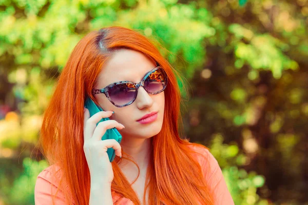 Serious red head woman talking at phone outdoors park green tree — 스톡 사진