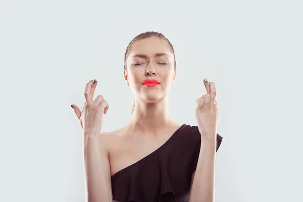 Primer plano retrato de una hermosa mujer de ensueño con el hombro abierto vestido negro de pie cruzando los dedos con los ojos cerrados quería hacer realidad sus deseos. Aislado sobre fondo blanco azul claro —  Fotos de Stock