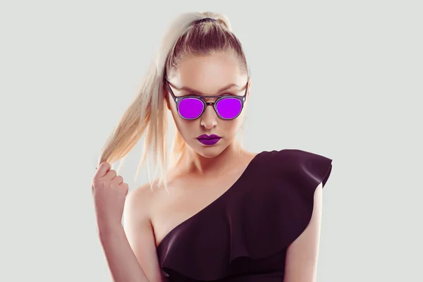 Me encanta el púrpura. seguro de éxito hermosa atractiva joven chica de moda con gafas de sol de color rosa y lápiz labial tirando de pelo de cola de caballo mirándote cámara seria aislado fondo gris — Foto de Stock