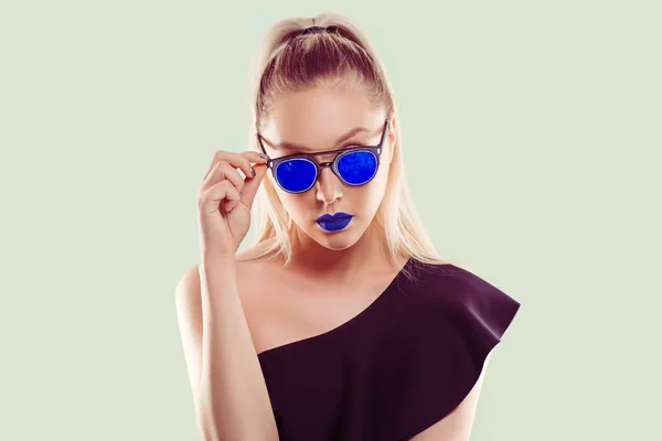 Moda în albastru. O femeie frumoasă care deține ochelari de soare albaștri în combinație cu rujul ei albastru izolat fundal verde deschis — Fotografie, imagine de stoc