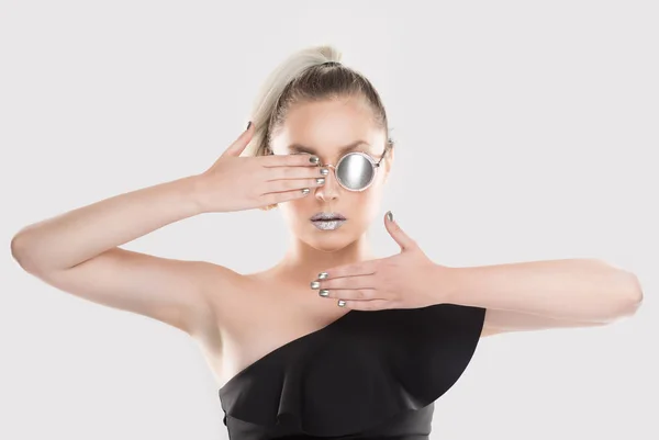 Look at my metallic shiny mirror style effect. Girl showing her combined set of grey sunglasses nails lipstick. Stylish woman holds right hand on the eye left hand near chin isolated white background