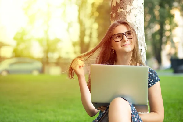Soñando despierto sobre el futuro. Mujer pensativa adolescente mujer con una computadora portátil sentada cerca de un árbol en un césped verde césped aislado ciudad parque campus fondo — Foto de Stock