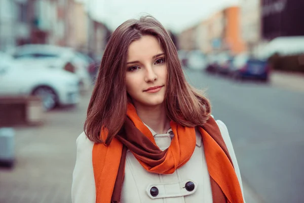 Attractive serious young Vietnamese woman in beige jacket coat and vivid red scarf isolated in an urban street looking at the camera you, close up view of her face and shoulders. Mixed race model — Stock Photo, Image
