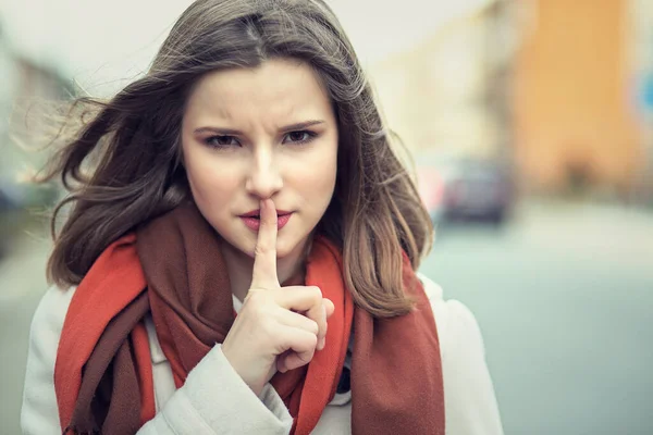 Shh Woman wide eyed asking for silence or secrecy with finger on lips hush hand gesture cityscape outdoor background Pretty girl placing fingers on lips sign symbol. Negative emotion facial expression