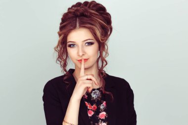 Sessiz ol. Kadın sessizlik ya da gizlilik istiyor parmakları dudaklarında el hareketi açık yeşil arka plan duvarı. Güzel kız parmaklarını dudaklarına koyuyor, 