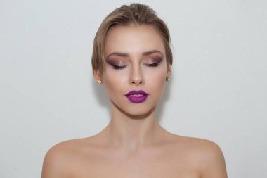 Gözleri kapalı, makyajlı, mükemmel bir cilde sahip genç bir kızın yakın plan portresi. İzole edilmiş açık mavi gri duvar arkaplanı.