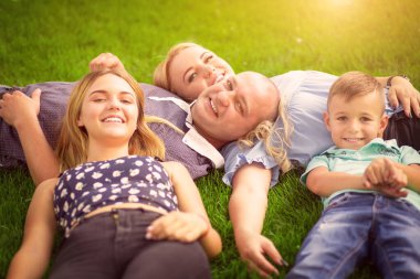 Mutlu aile kavramı. Anne, baba, güneş ve kız açık havada çimenlerin üzerinde uzanıyor. Güneşli bir günde güneş parlıyor.. 