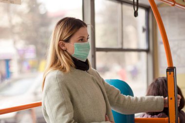 Koronavirüse karşı steril koruyucu tıbbi maske takan kadın, Avrupa 'nın bir caddesinde halk otobüsüne binerken Covid-2019 Asya pandemik sarar virüsü, arka plandaki insanlar...