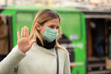 Steril koruyucu tıbbi maske takan genç bir kadın doktor, onu durduruyor. El işaretleriyle işaret veriyor. Şehrin arka planında virüse hava yoluyla yakalanmayı reddeden biri yok.