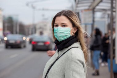 Koronavirüse karşı steril koruyucu bir maske takan neşeli bir kadın, Avrupa 'nın otobüs durağındaki halk otobüsünde Covid-2019 Asya pandemik sarar virüsü kameramanların geçmişine bakıyor.