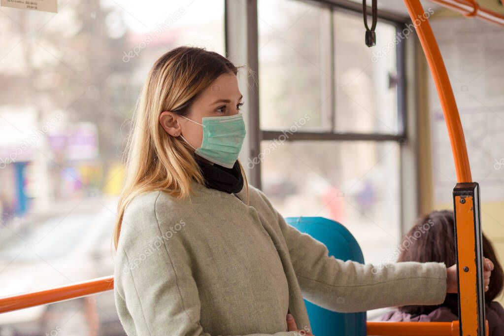 Woman wearing a sterile protective medical mask against coronavirus, Covid-2019 Asian pandemic sars virus while going in a public bus in a European city street looking ahead, people on the background