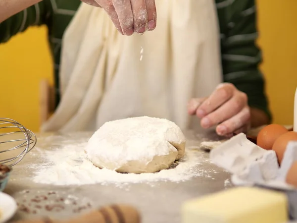 Male hands, chef adding salt and flour to dough working on it on a gray stone table