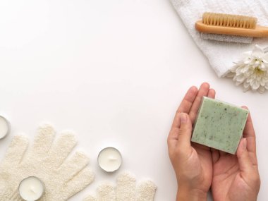 Spa seti. Yeşil, doğal sabun çubuğu, tahta, kireç taşı, mum, havlu, fotokopi alanı olan açık beyaz arka planda çiçek tutan eller. Hijyenik banyo aletleri konsepti. Üst Manzara, düz uzanma