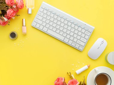 Klavye faresi, bir fincan çay ve makyaj malzemesi ve çevresindeki kozmetik ürünler sarı arka planda izole edilmiş. Düz konum, üst görünüm kopyalama alanı. Kadınsı güzellik blogcusu iş yeri kavramı.