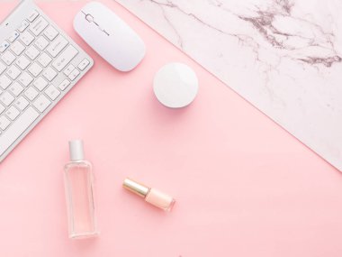 Düz, pembe masa çerçevesinin üst görüntüsü. Dizüstü bilgisayarı, iyileştirici kozmetik ürünleri, tırnak cilası, parfümü, bilgisayar klavyesi ve faresi olan kadın çalışma alanı kopyalama alanı olan pembe bir arka planda izole edilmiş..