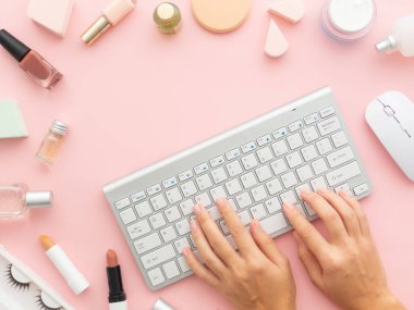 Doğal kozmetik ürünlerini internetten sipariş et. Nemlendirici yüz kremi şişeleri, oje, takma kirpikler, ruj, pembe arka planda izole edilmiş bir klavye faresi. Düz görünüm kopyalama alanı