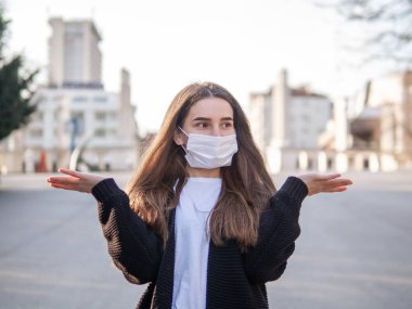 Kafası karışmış, omuzlarını silken, tıbbi maske takan, kafası karışmış bir kadının portresi şehirde dikilen yüz ifadesiyle karşılaşıyor. Koronavirüsten korunma.