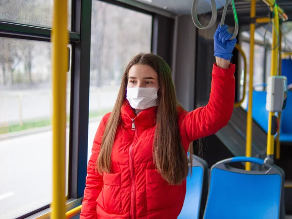Woman wearing a sterile protective medical mask and gloves against coronavirus, Covid-2019 Asian pandemic virus while going in a public bus in a European city street looking ahead, bus on background