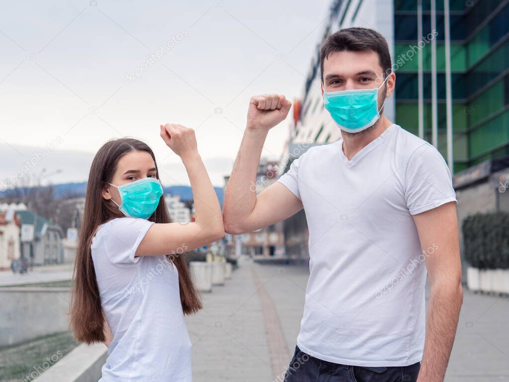 Elbow bump. Two people woman, man wearing medical mask, friends greet each other with elbows, instead of shaking hands looking at camera showing the new greeting way to avoid the spread of coronavirus