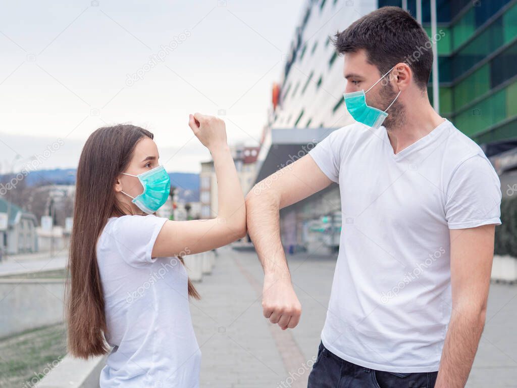 Two people woman and man wearing medical mask, friends greet each other with their elbows, instead of shaking hands. Elbow bump. A new greeting way to avoid the spread of coronavirus.